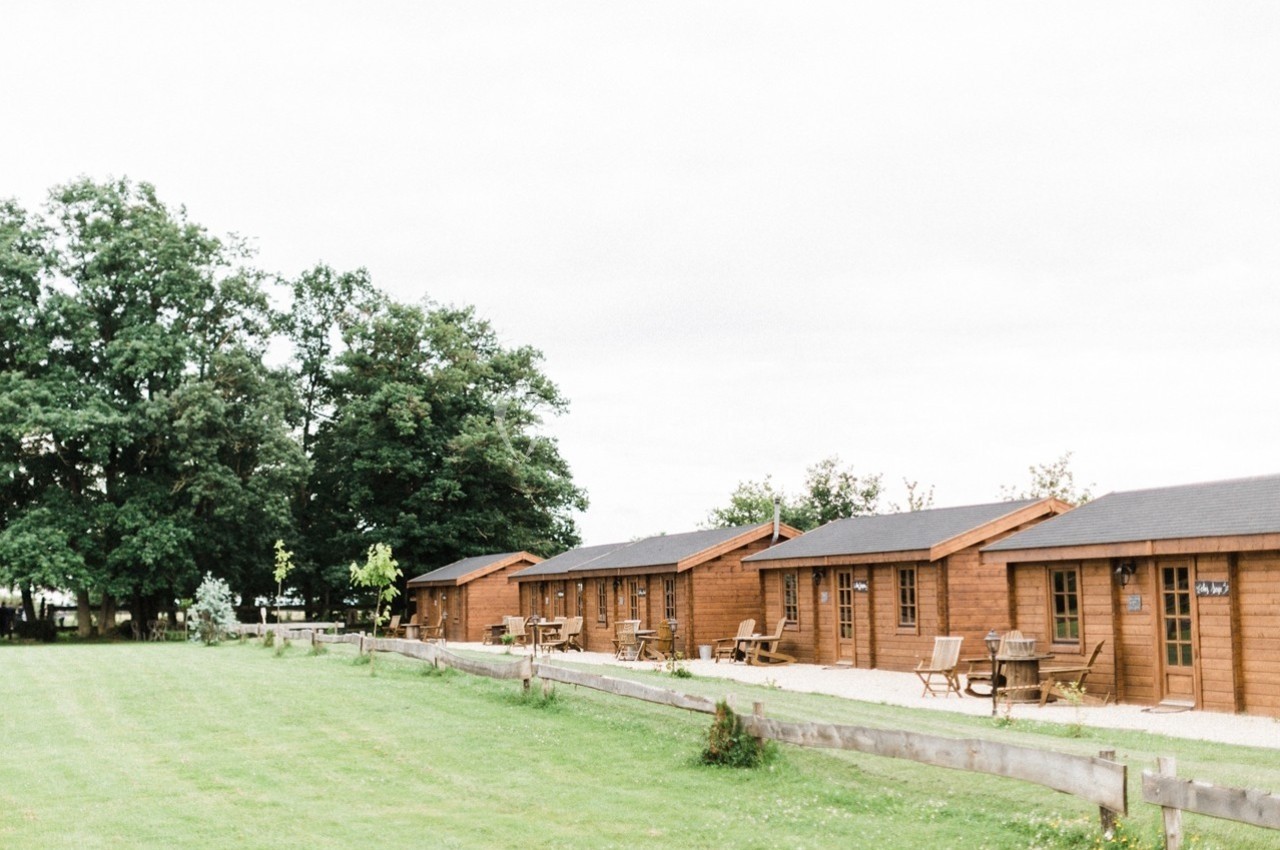 Alignement de chalets en bois avec terrasses, entourés d'une pelouse et d'arbres sous un ciel nuageux.