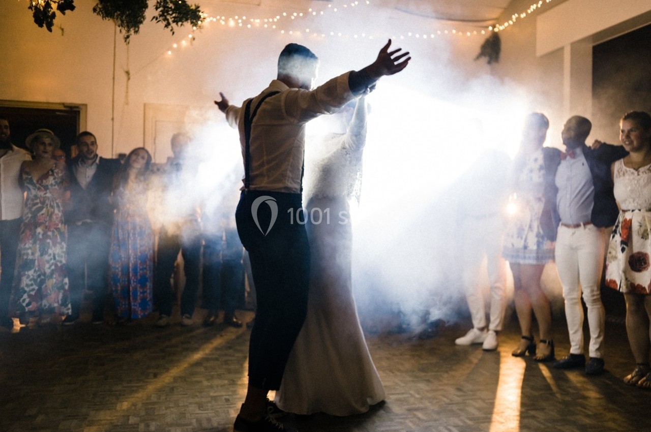 Un couple danse au centre d'une salle éclairée, entouré d'invités et d'une ambiance lumineuse et festive.