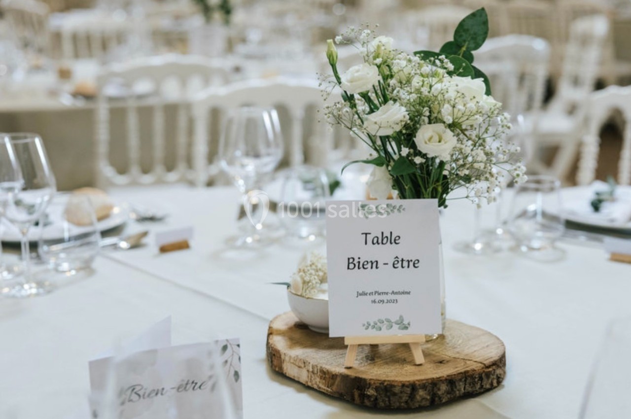 Centre de table avec fleurs blanches et panneau ’Table Bien-être’ sur une rondelle de bois, dans une salle de réception.