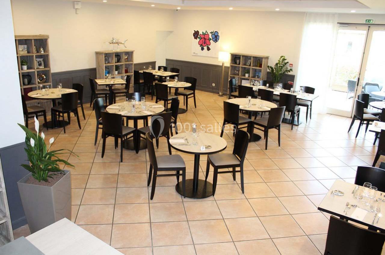 Salle de restaurant lumineuse avec des tables rondes dressées, des chaises noires et des étagères en arrière-plan.