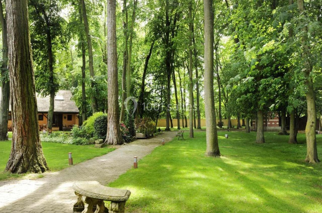 Allée pavée bordée d'arbres et de pelouse menant à une maison en bois dans un cadre forestier.