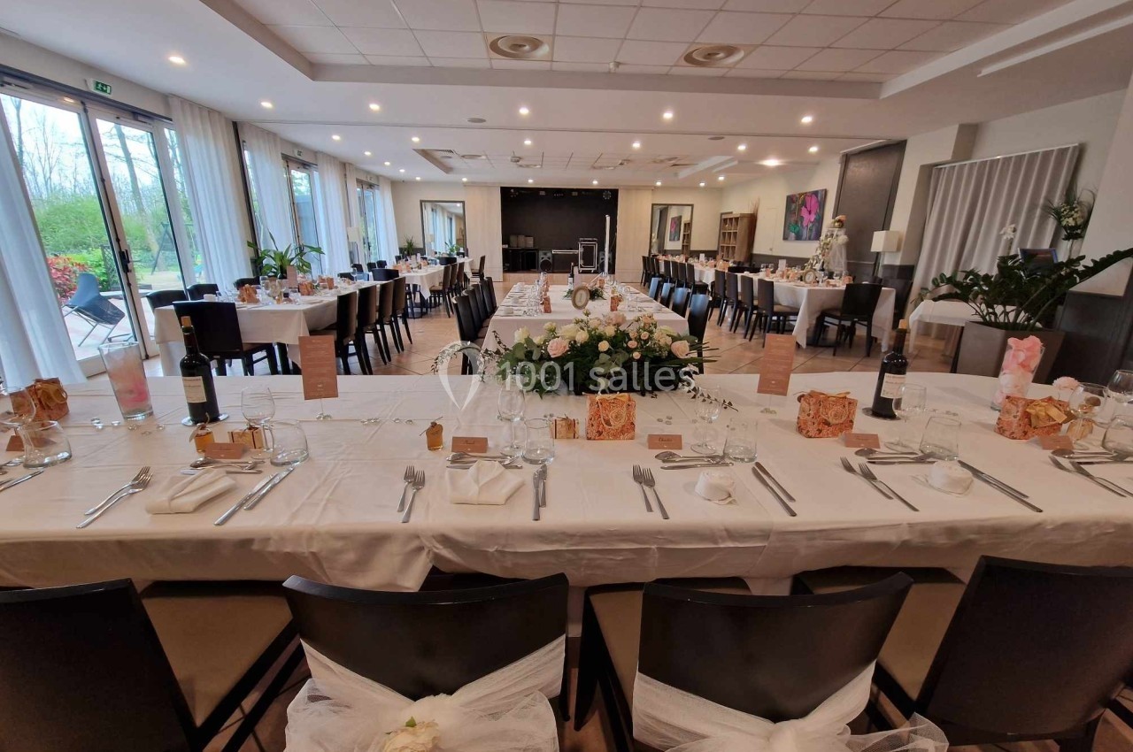 Salle de réception décorée pour un événement, avec tables dressées, nappes blanches et arrangements floraux centraux.