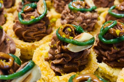 Choux noirs garnis de crème blanche et décorés de filet de caramel, disposés sur une surface métallique.