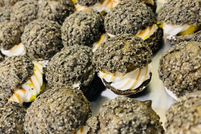 Choux noirs garnis de crème blanche et décorés de filet de caramel, disposés sur une surface métallique.