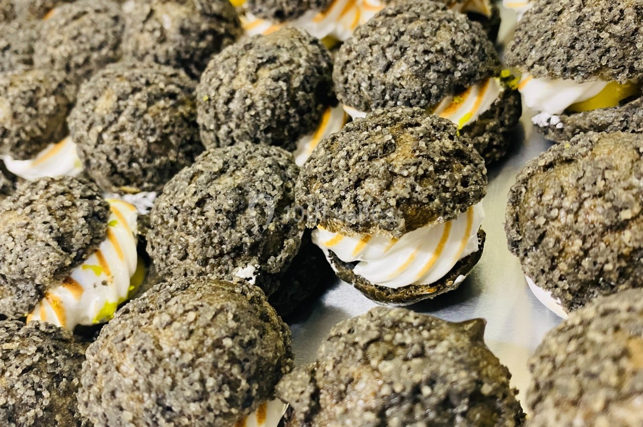 Choux noirs garnis de crème blanche et décorés de filet de caramel, disposés sur une surface métallique.