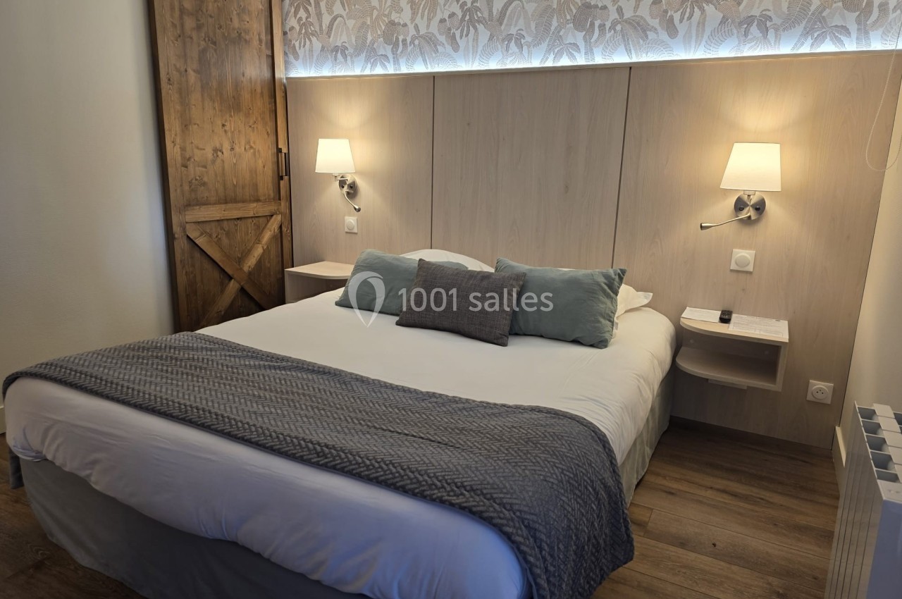 Lit double avec coussins et plaid gris dans une chambre au décor sobre, éclairée par deux appliques murales.