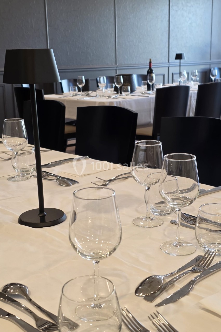 Tables de restaurant élégamment dressées avec nappes blanches, verres, couverts et lampes noires.