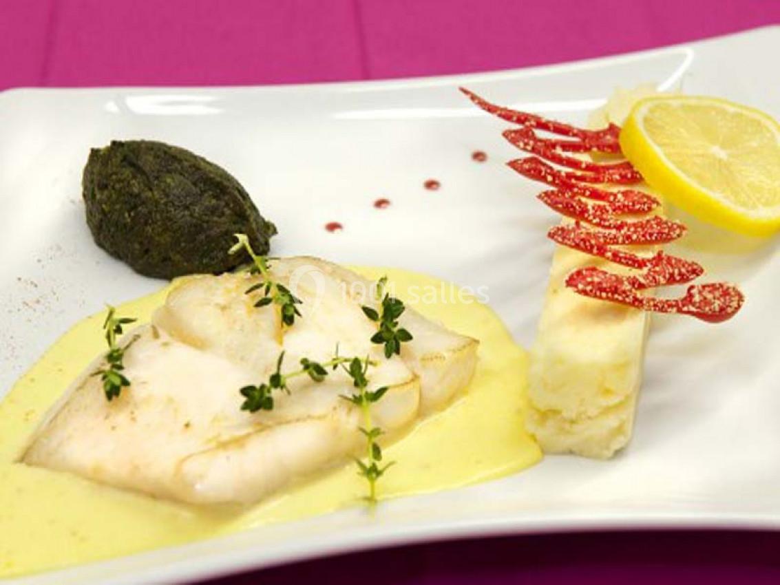 Filet de poisson sur sauce jaune, accompagné de purée verte, d'une garniture rouge et d'une tranche de citron.