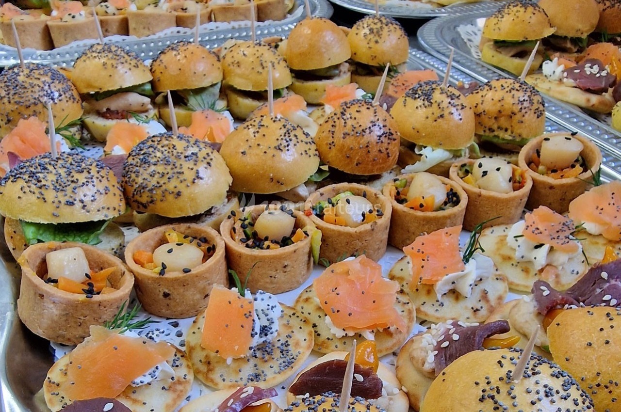 Plateaux garnis de bouchées variées, incluant mini-burgers, canapés au saumon et amuse-bouches garnis de graines.