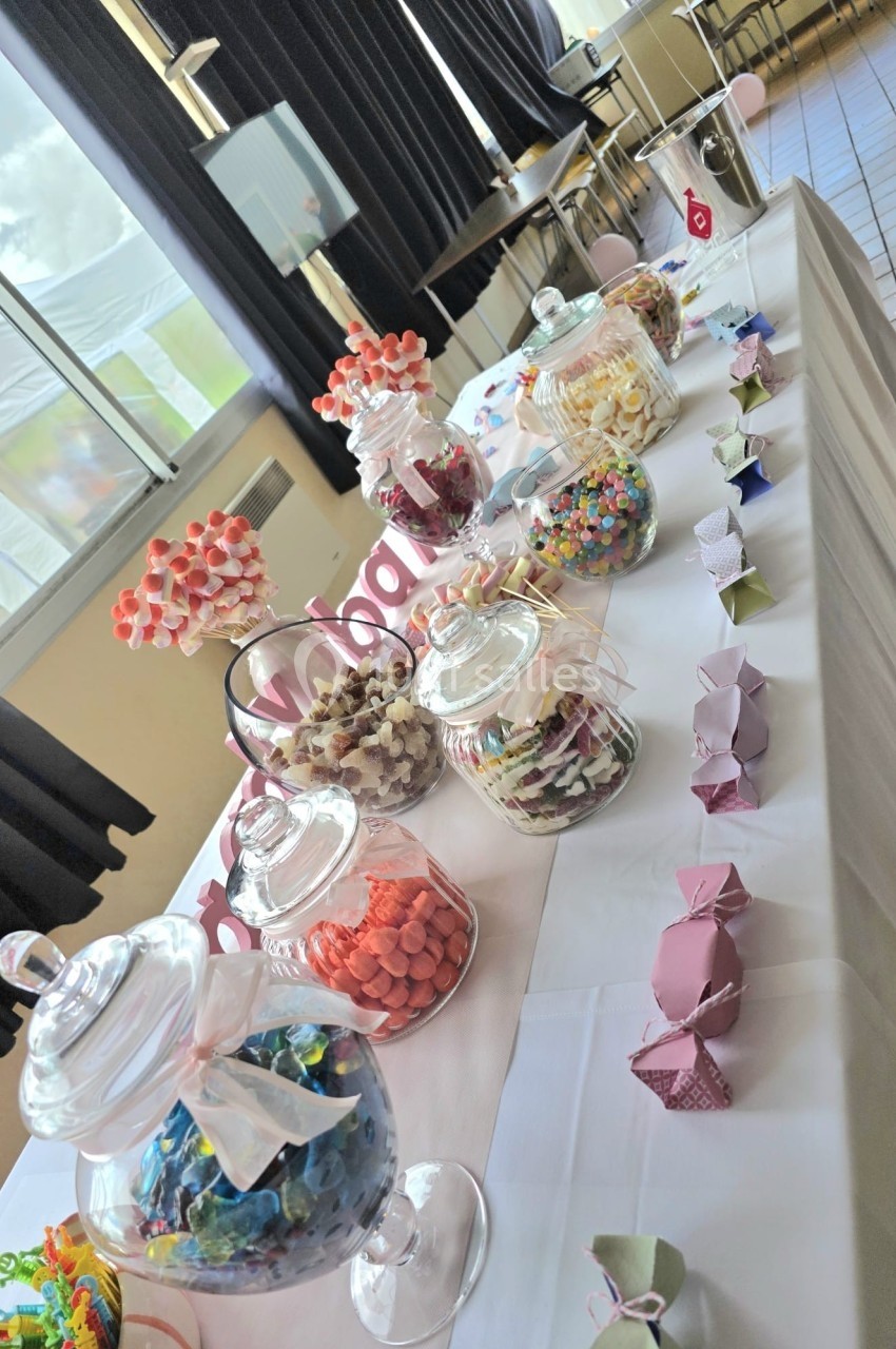 Table décorée avec des bonbonnières remplies de sucreries colorées et pliages en papier, dans une salle lumineuse.