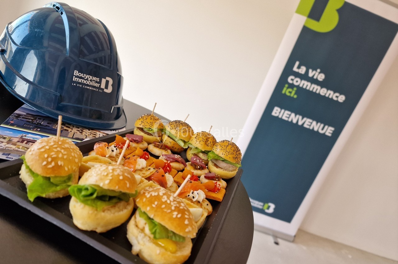 Plateau de mini-burgers et amuse-bouches devant un casque de chantier et un panneau d'accueil d'une entreprise.