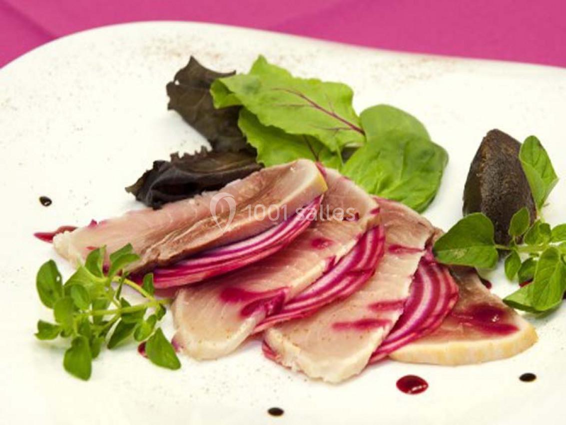 Tranches de poisson cru accompagnées de betteraves, feuilles de salade et herbes fraîches sur une assiette blanche.