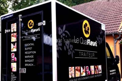 Camion noir de traiteur ’Le Quai Fleuri’ garé devant un bâtiment, avec des visuels de prestations culinaires.
