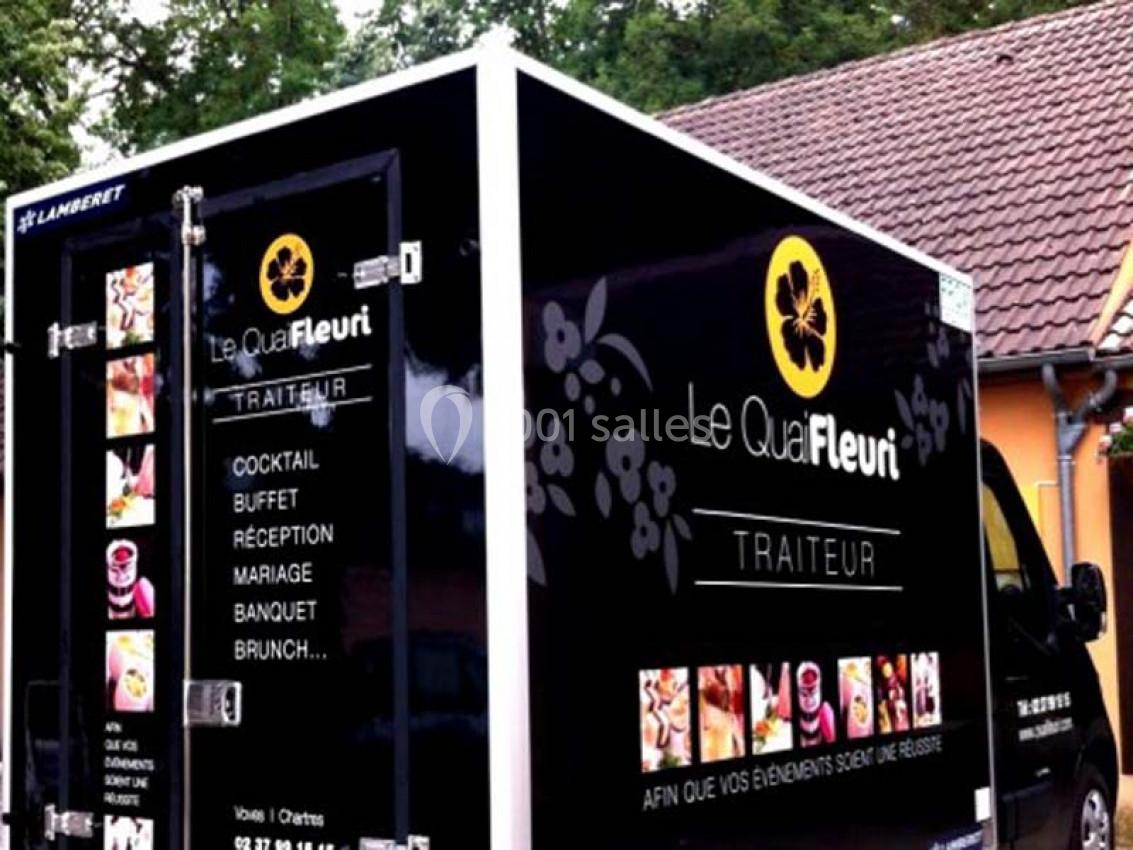 Camion noir de traiteur ’Le Quai Fleuri’ garé devant un bâtiment, avec des visuels de prestations culinaires.