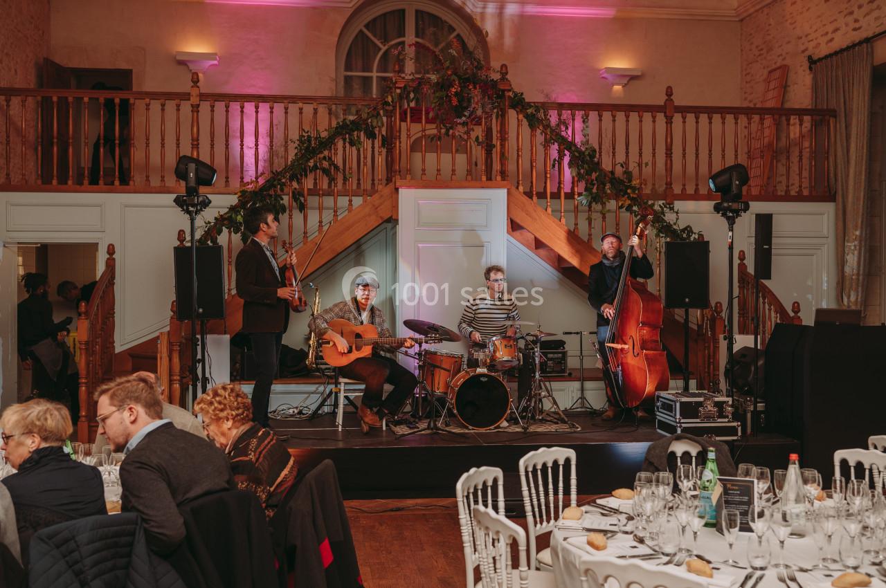 Un groupe de musiciens joue sur une scène dans une salle décorée, avec des invités assis à des tables.