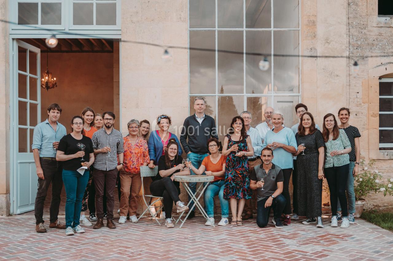 Un groupe de personnes posant devant un bâtiment en pierre avec des portes vitrées et une terrasse en briques.