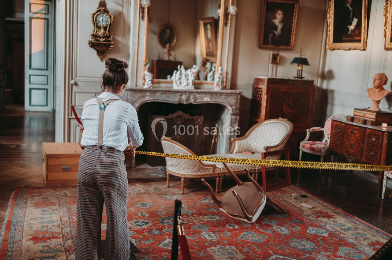 Une femme observe une scène barricadée dans une pièce ancienne avec des meubles renversés et des œuvres d'art.