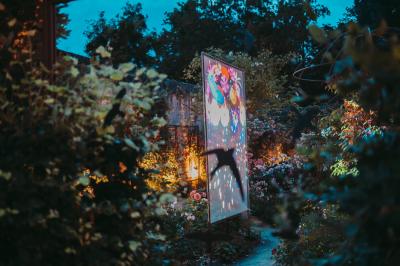 Écran lumineux affichant des images colorées dans un jardin fleuri à la tombée de la nuit.