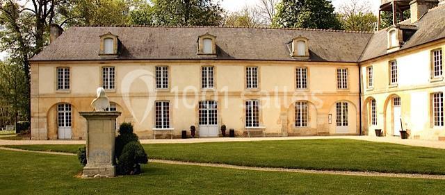 Façade d'un bâtiment ancien en pierre avec des fenêtres cintrées, entouré d'une pelouse et d'arbres.