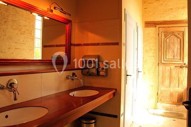 Salle de bain avec deux lavabos, miroir encadré en bois, mur clair et porte en bois au fond.