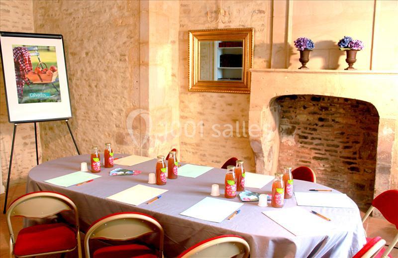Salle de réunion avec table ovale, chaises rouges, bloc-notes, bouteilles de jus et chevalet avec affiche.