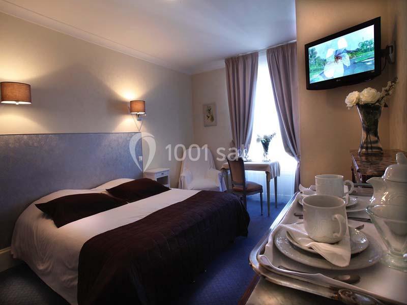 Chambre lumineuse avec lit double, table dressée près d'une fenêtre, télévision murale et plateau de courtoisie.