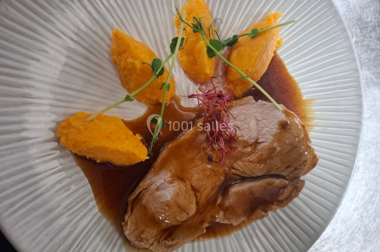 Assiette avec des tranches de viande nappées de sauce, accompagnées de purée de carottes et décorées de pousses.