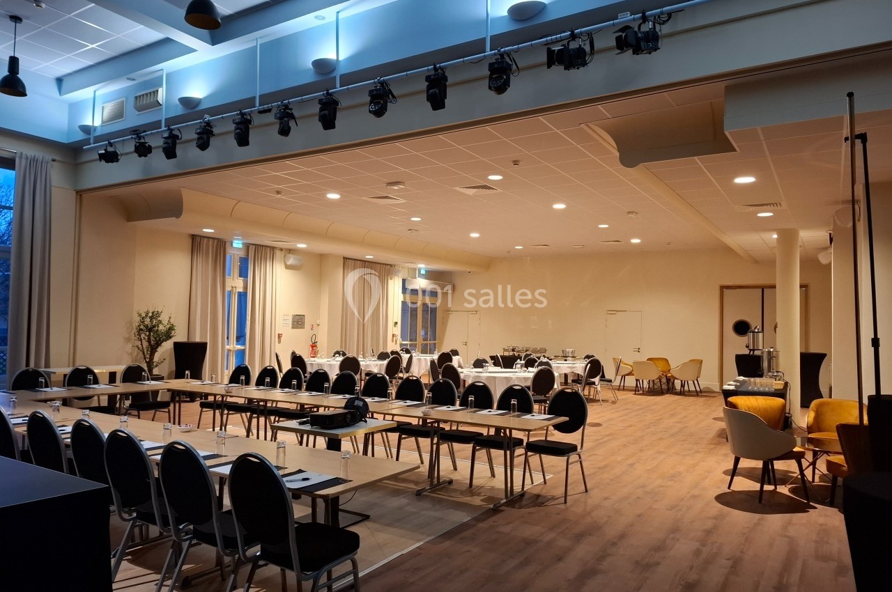 Salle de conférence lumineuse avec des tables disposées en U, des chaises alignées et un espace pour des présentations.