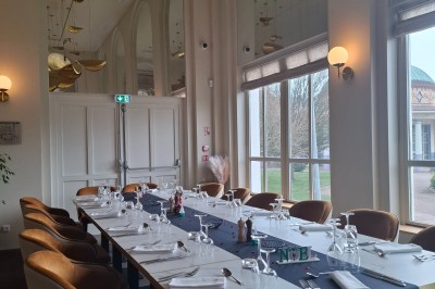 Salle de conférence lumineuse avec tables disposées en U, écran de projection et grandes fenêtres donnant sur l'extérieur.