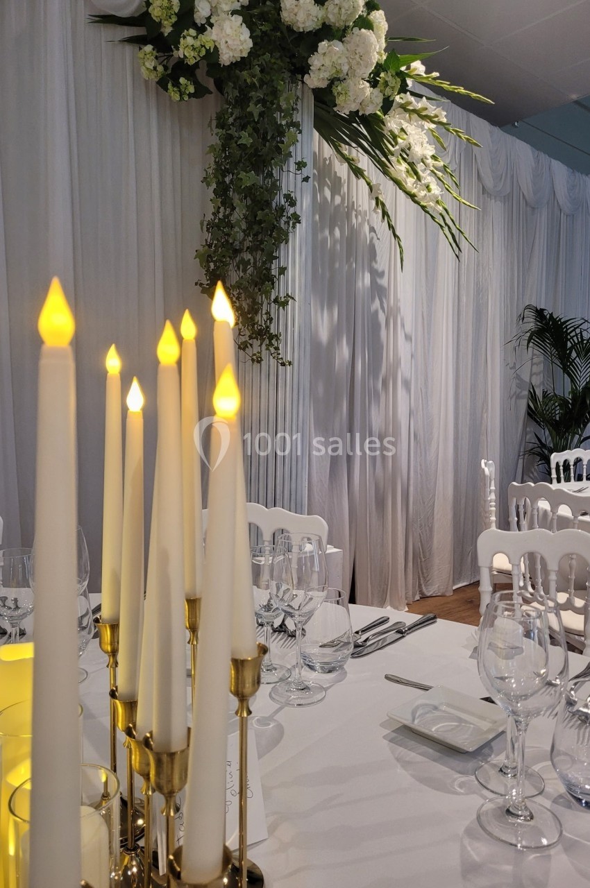 Bougies LED sur une table élégamment dressée, avec rideaux blancs et décor floral en arrière-plan.