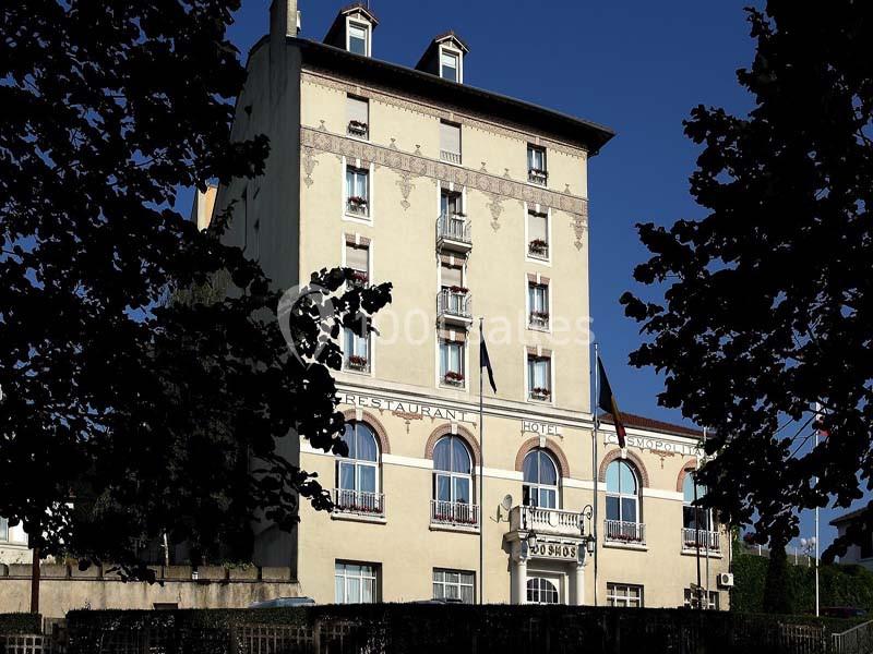 Façade d'un hôtel ancien à plusieurs étages, avec des fenêtres symétriques et un ciel bleu dégagé en arrière-plan.