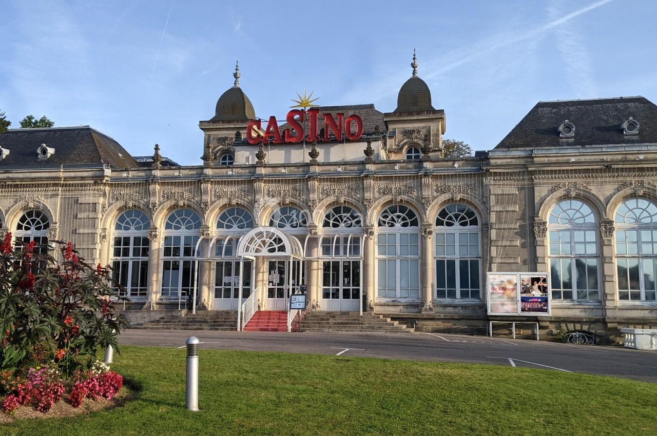 Façade d'un bâtiment historique abritant un casino, avec des jardins et une pelouse à l'avant.