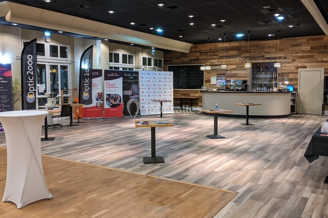 Salle d'exposition avec stands promotionnels, tables hautes et un bar en arrière-plan.