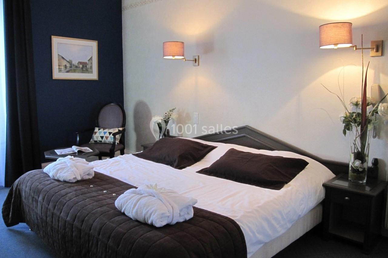 Chambre d'hôtel avec un grand lit, deux lampes murales, des peignoirs posés et une décoration sobre.