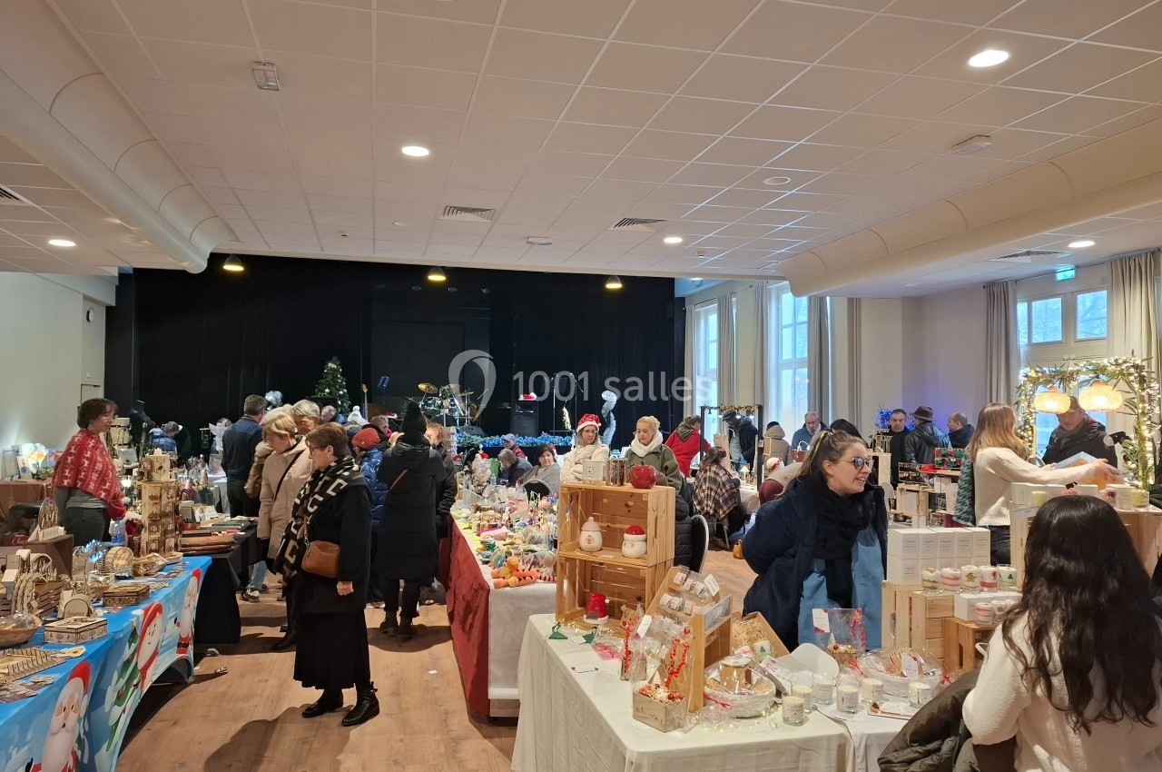 Des stands de marché de Noël en intérieur avec des visiteurs observant des produits artisanaux et décorations festives.