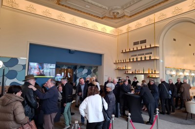 Tasse de café sur une table avec un macaron vert et un plateau de desserts flous en arrière-plan.