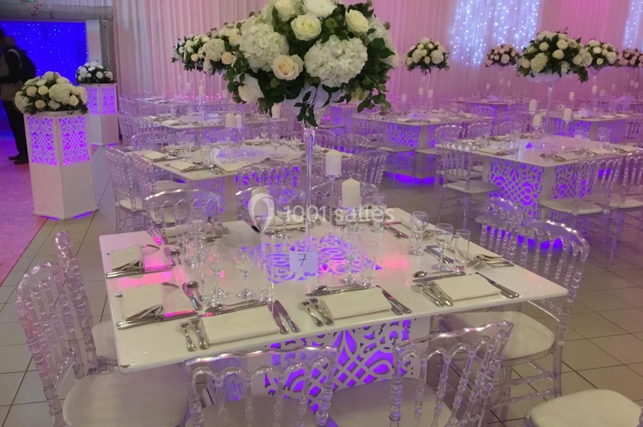 Salle de réception décorée avec des tables élégantes, chaises transparentes et centres de table fleuris.