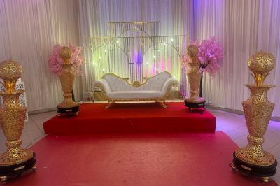 Canapé blanc orné sur une estrade rouge, entouré de colonnes dorées et de décorations florales roses.
