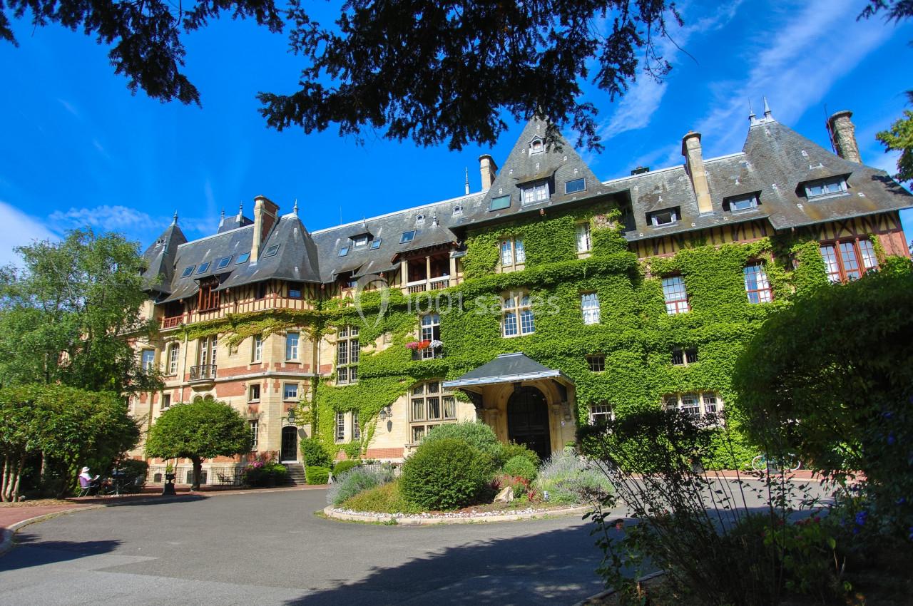 Façade d'un grand bâtiment ancien recouvert de lierre, entouré de végétation et sous un ciel bleu dégagé.