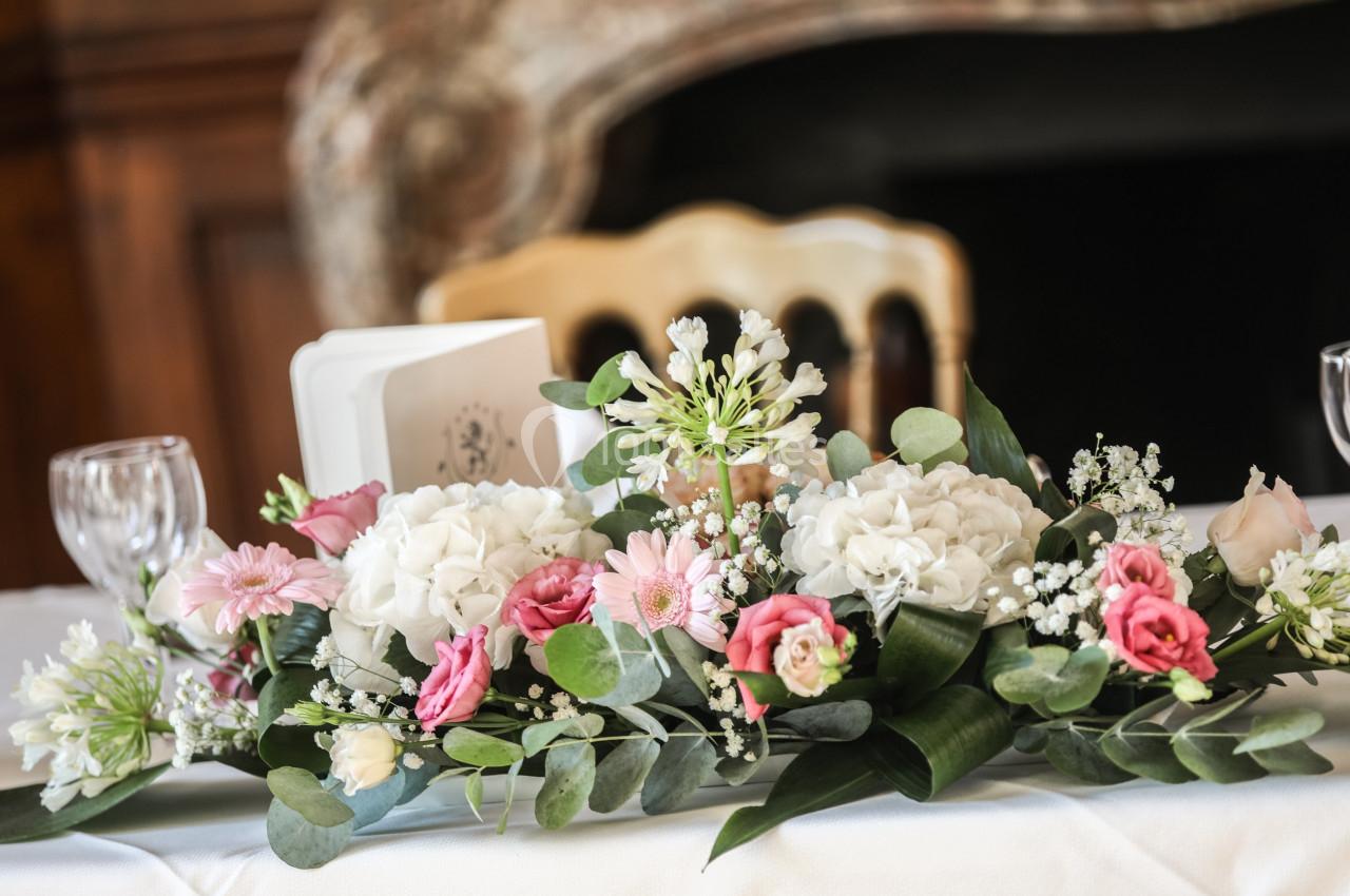 Centre de table floral avec roses, hortensias et feuillage, disposé sur une nappe blanche dans un cadre intérieur élégant.
