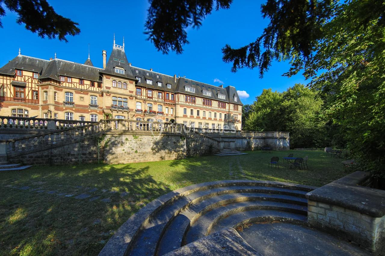 Façade d'un grand bâtiment historique entouré de verdure, avec des escaliers en pierre au premier plan.
