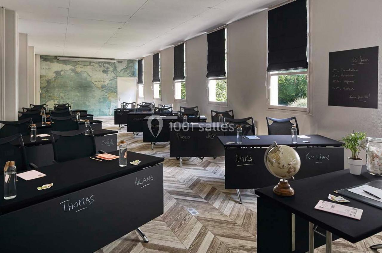 Salle de classe moderne avec des bureaux noirs personnalisés, un globe terrestre et une carte murale en arrière-plan.