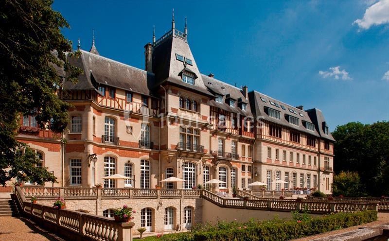 Façade d'un grand bâtiment historique avec toit en ardoise, entouré de verdure et baigné de lumière naturelle.