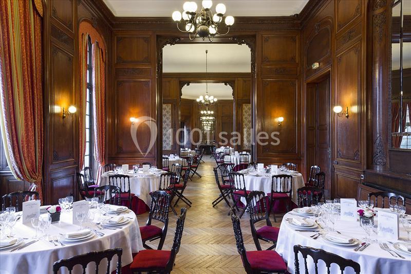 Salle élégante avec boiseries, tables rondes dressées pour un repas, chaises noires et lumière naturelle.