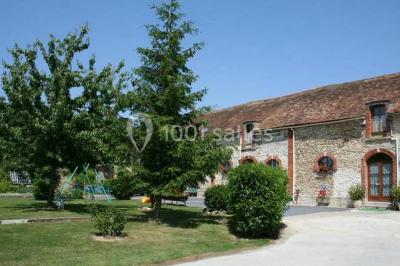 Espace extérieur avec balançoire, table et chaises blanches, parterre de fleurs rouges et jouet en plastique jaune.