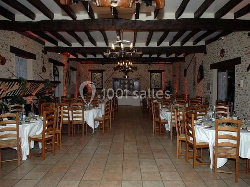 Salle de réception avec tables dressées, chaises en bois, poutres apparentes et murs en pierre.