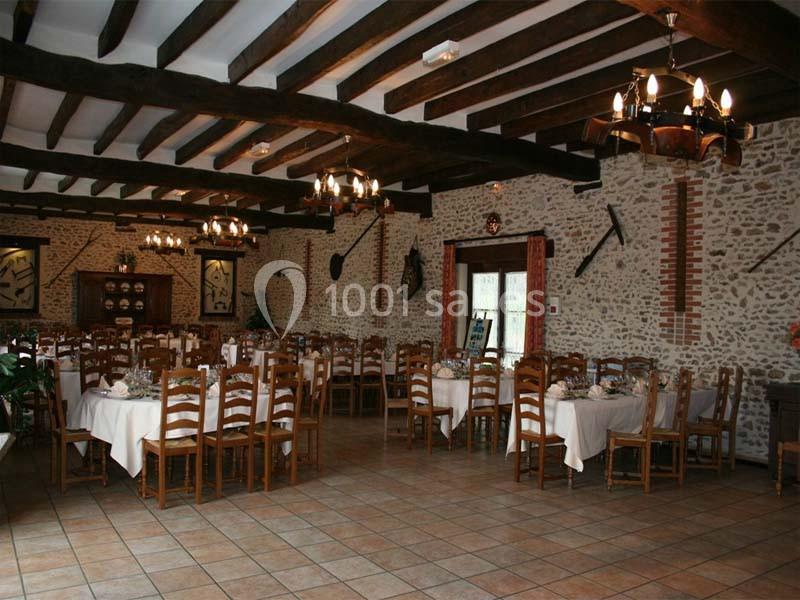 Salle de réception rustique avec murs en pierre, poutres apparentes, tables dressées et chaises en bois.