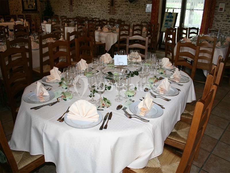 Table ronde élégamment dressée avec nappes blanches, serviettes pliées, couverts et verres dans une salle de réception…
