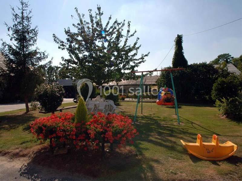 Espace extérieur avec balançoire, table et chaises blanches, parterre de fleurs rouges et jouet en plastique jaune.