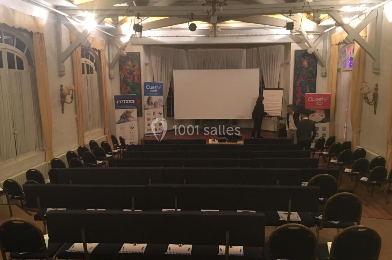 Salle de conférence avec des rangées de chaises, un écran de projection et des affiches promotionnelles en arrière-plan.